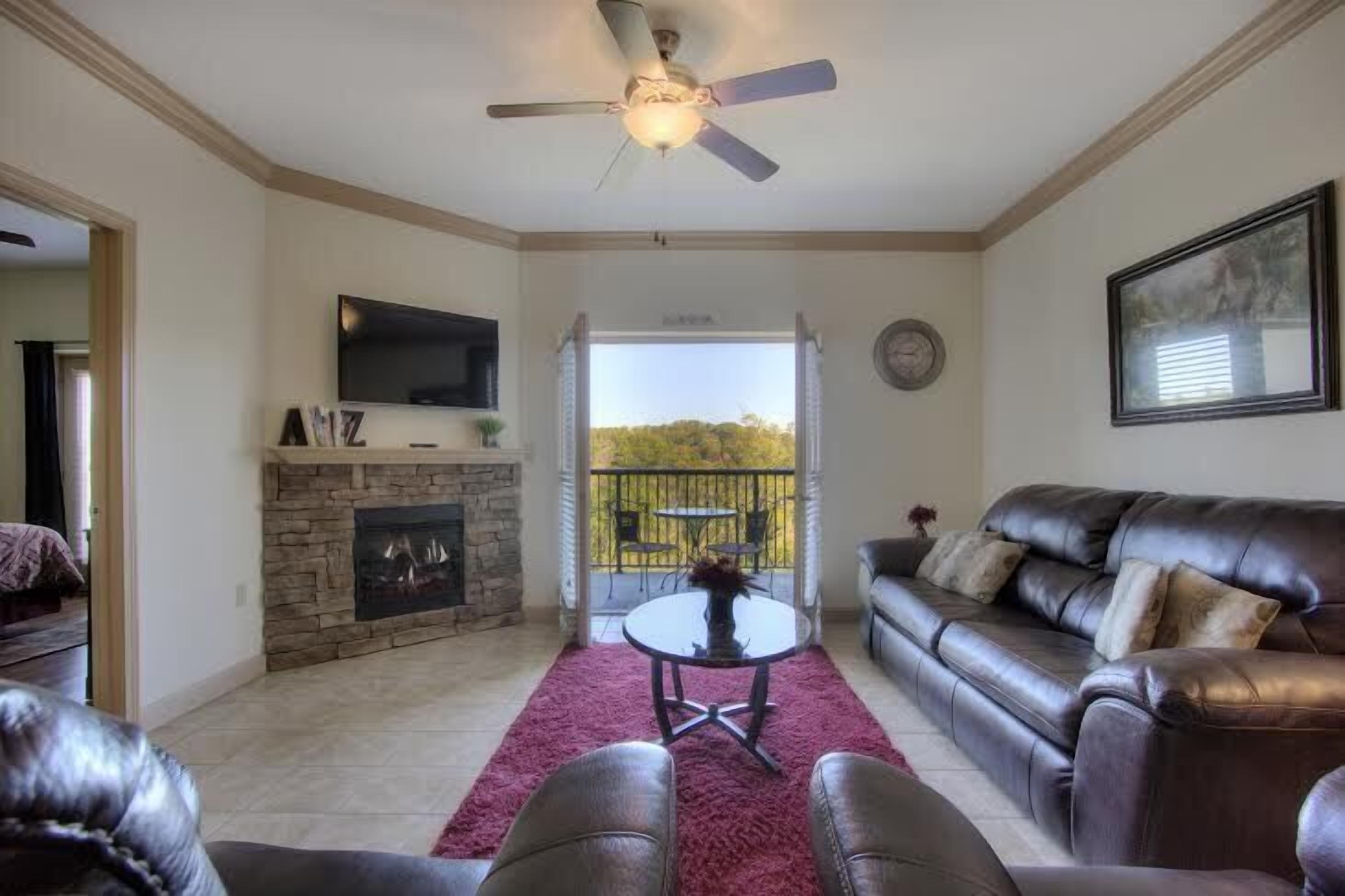 A living room with a stone fireplace, leather sofa, and a ceiling fan.