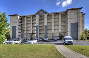 A multi-story hotel with a central entrance, parking lot, and several vehicles parked in front. - John's Mtn Blessing  w/ 2 Pools, Hot tub, Arcade Games 7 BR & 6 BA.  Sleeps 20+ (Pigeon Forge)