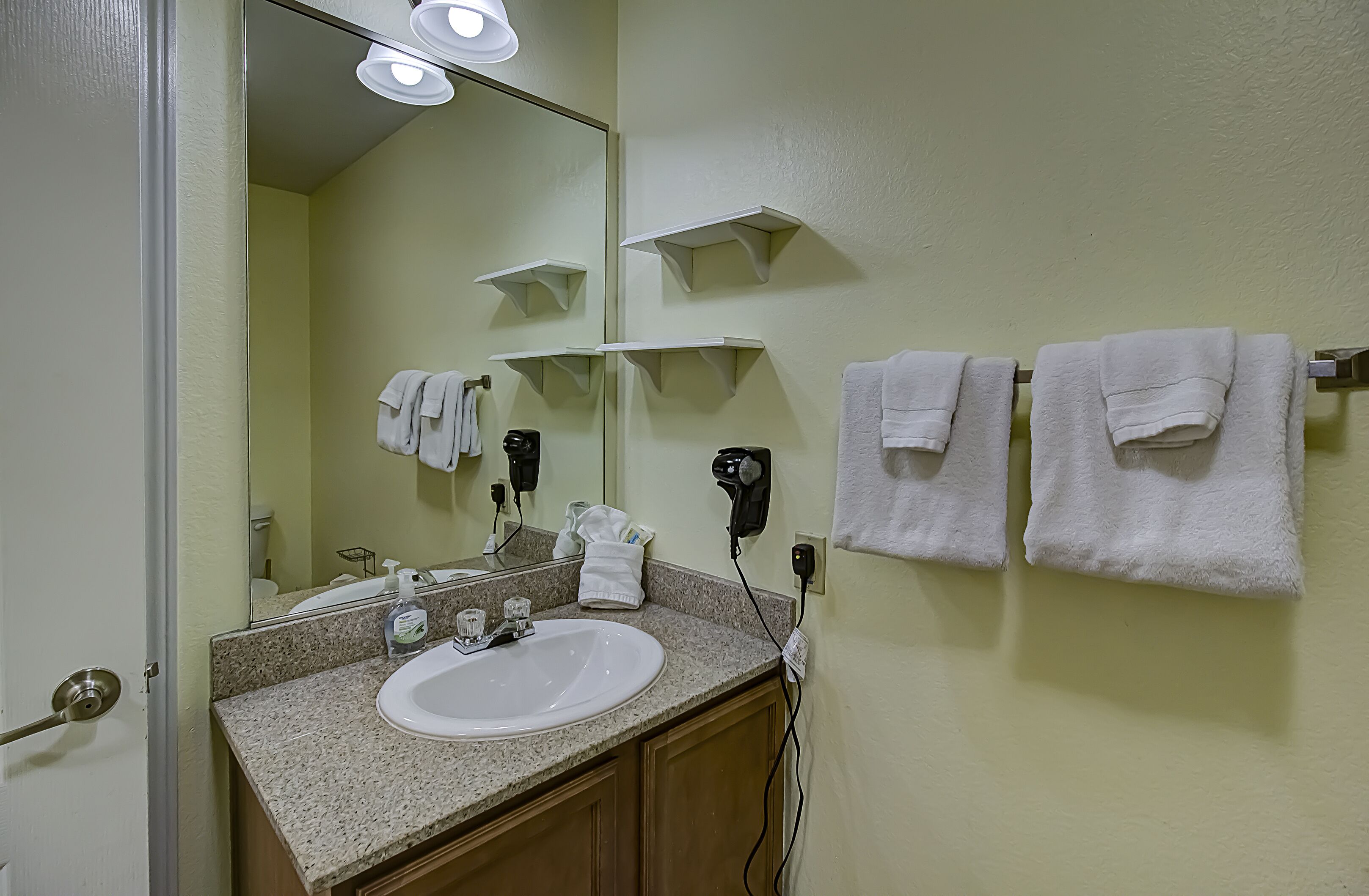 A bathroom with a sink, mirror, towel rack, and a hairdryer on the wall.
