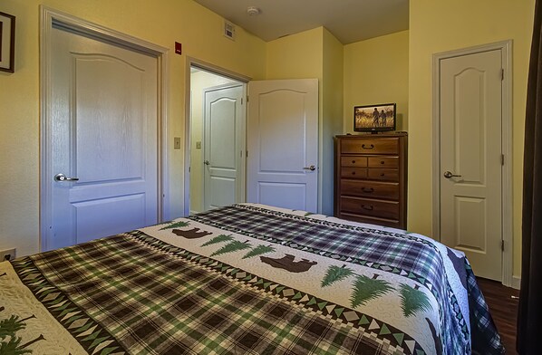 Ein Schlafzimmer mit einem Bett, zwei Türen, einer Kommode und einem gerahmten Bild auf der Kommode.