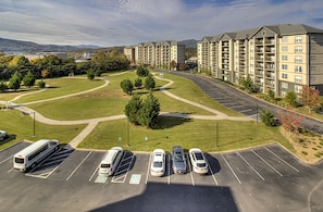 A parking lot with several cars and a bus, surrounded by a landscaped area with trees and a view of apartment buildings. - John's Mtn Blessing  w/ 2 Pools, Hot tub, Arcade Games 7 BR & 6 BA.  Sleeps 20+ (Pigeon Forge)