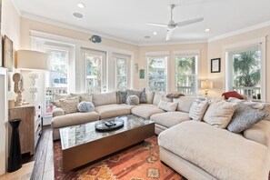 A modern living room with a beige sectional sofa, a glass coffee table, and a ceiling fan.