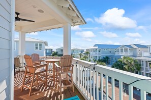 A balcony with wooden chairs and a table, overlooking a row of houses with a clear sky.