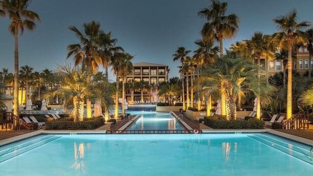 Una piscina rodeada de palmeras y sillas de descanso, con un edificio al fondo.