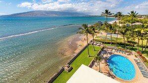 A beach resort with a swimming pool, palm trees, and a view of the ocean. - Oceanfront 2BR_2BA Kihei Maui–Stunning Lanai Sunsets, Beach Front, Turtles! (Kihei)