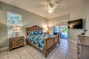 A bedroom with a bed, a nightstand, a lamp, a ceiling fan, a TV, and a window with blinds.