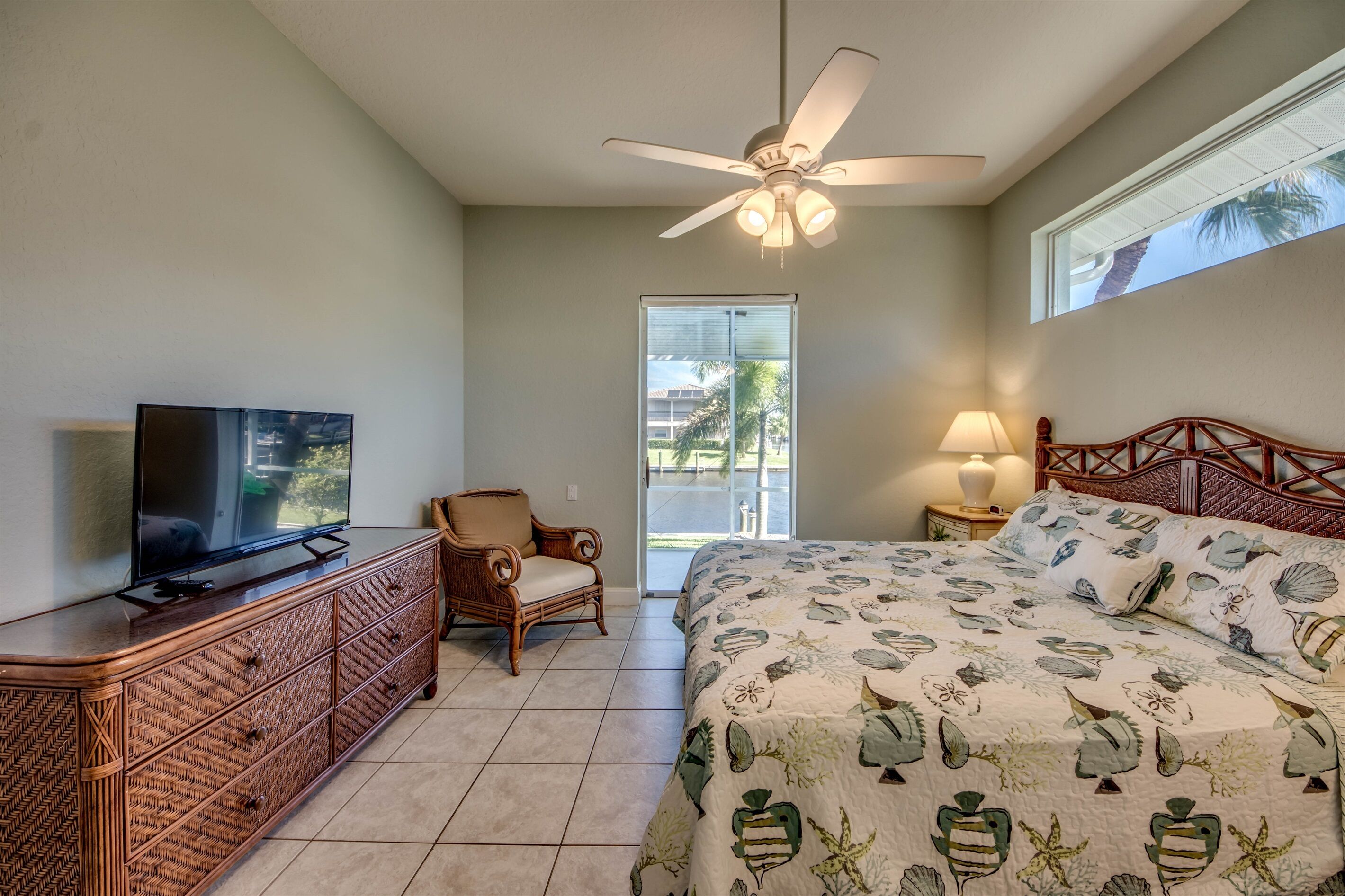 A bedroom with a bed, a television on a dresser, a chair, a ceiling fan, and a window.