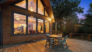 A wooden cabin with large windows, a deck, and outdoor seating. - Cliffside Escape | Epic Lake Views & Off-Grid Stay (Broken Bow)