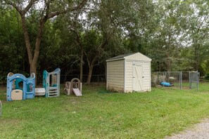 Enjoy a serene backyard with a storage shed and play area featuring a slide and climbing structure amidst lush greenery.