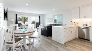 A modern kitchen with white cabinets, a central island, and a dining area with white chairs.