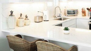 A modern kitchen with white cabinets, a marble countertop, a toaster, and wicker bar stools.