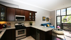 A modern kitchen with dark wood cabinets, stainless steel appliances, and a large window providing a view of the outdoors. - Luxury Condo in Santana Row - Silicon Valley - Levi's Stadium (San Jose)