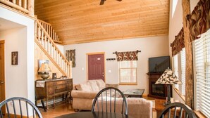 A cozy living room with a wooden ceiling, a sofa, a dining table, and a staircase.