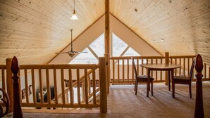 A cozy attic bedroom with a wooden ceiling, a wooden railing, a round table, and a single bed.