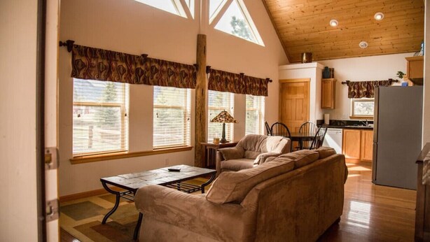 A spacious living room with a large sofa, a dining table, and a kitchen area with wooden cabinets and a refrigerator.