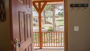 An open wooden door leading to a covered outdoor area with a wooden railing, a hanging light fixture, and a wall-mounted hookboard.