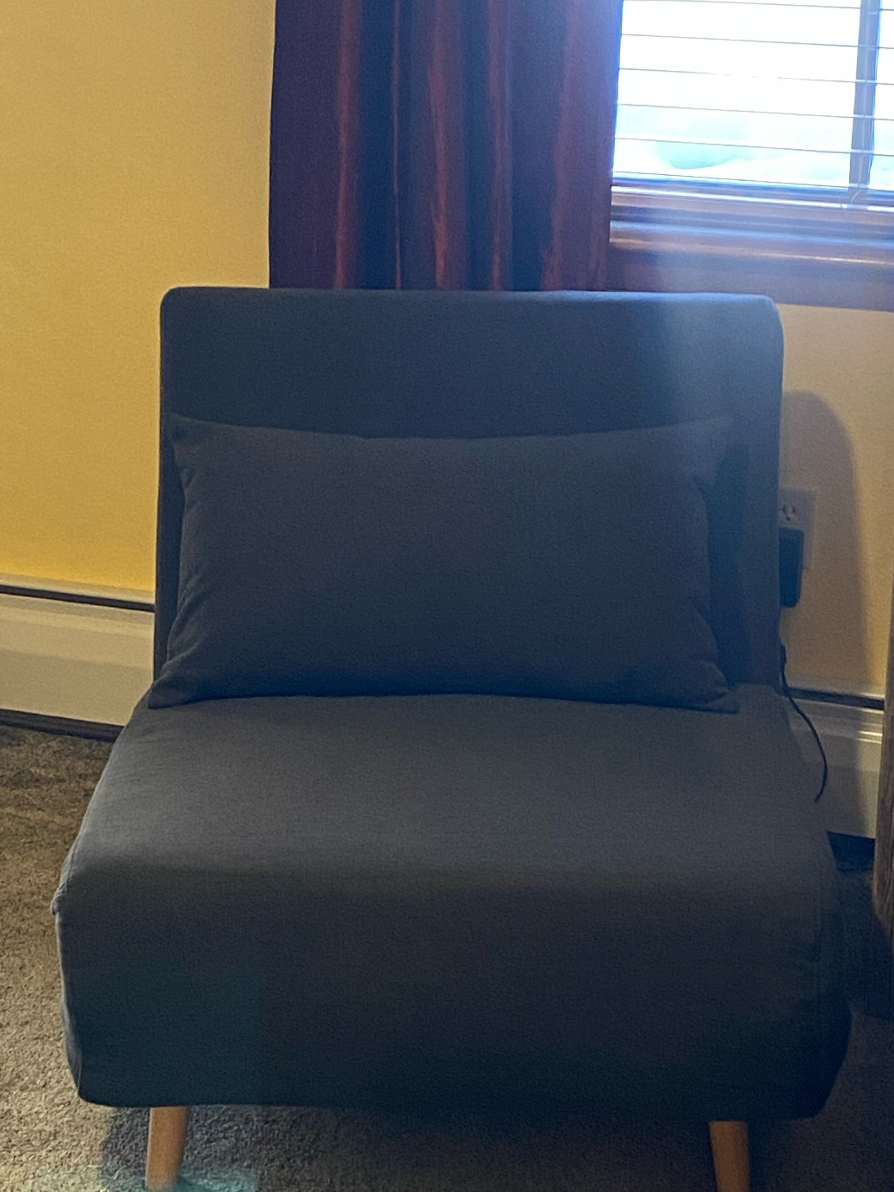 A dark-colored sofa with wooden legs in a room with yellow walls and a window with blinds.