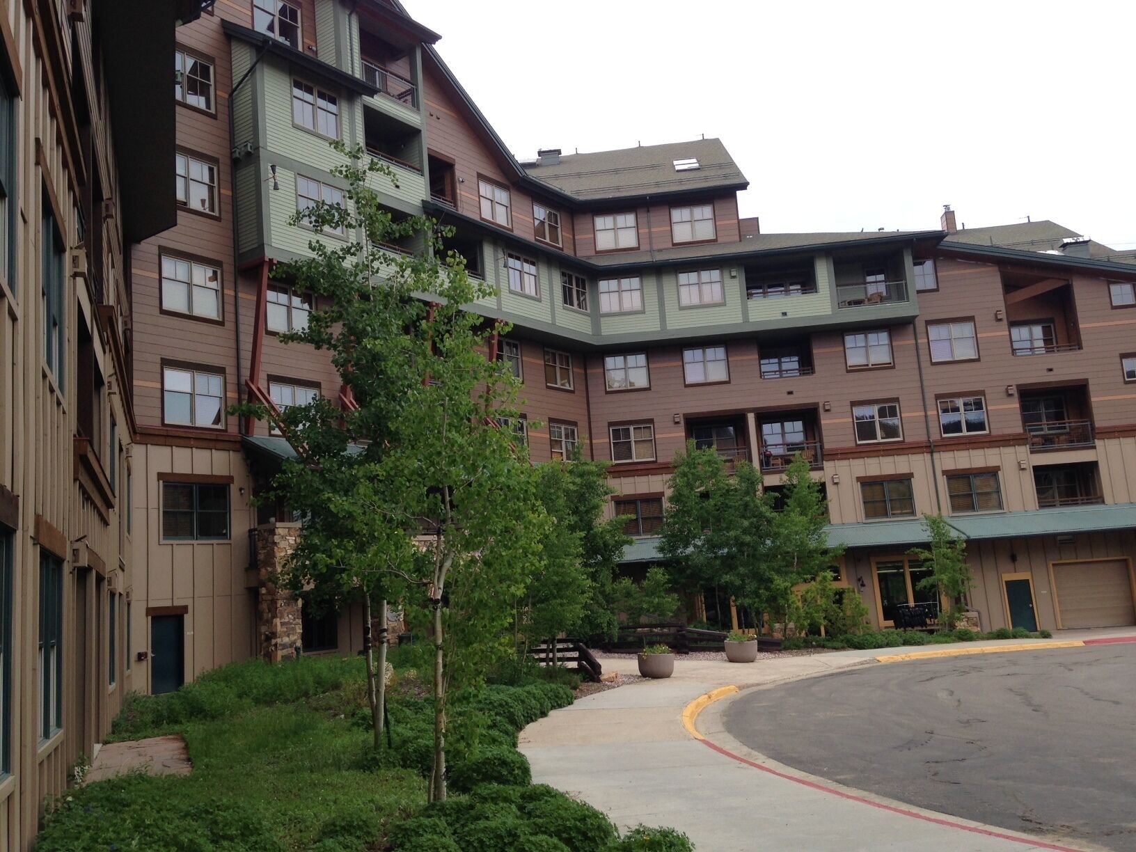 A multi-story residential building with a mix of balconies and windows, surrounded by greenery and a curved driveway.