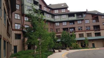 A multi-story residential building with a mix of balconies and windows, surrounded by greenery and a curved driveway.