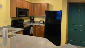 Una cocina con armarios de madera, un refrigerador negro, un microondas, un horno y una cafetera.