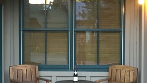 Una pequeña zona de estar al aire libre con dos sillas de madera y una mesa redonda, con una botella de vino.