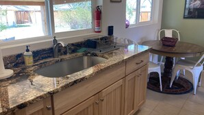 Eine Küche mit Granit Arbeitsplatten, Holzschränken, einer Edelstahlspüle und einem Essbereich mit rundem Tisch und Stühlen.