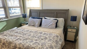 Ein Schlafzimmer mit einem Bett, zwei Nachttischen und einem Fenster mit Jalousien.