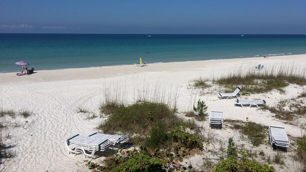 A beach with white sand, clear blue water, and a few beach chairs and umbrellas. - Gulf side! No crossing the street to get to the beach! COQUINA BEACH CLUB 109 (Bradenton Beach)