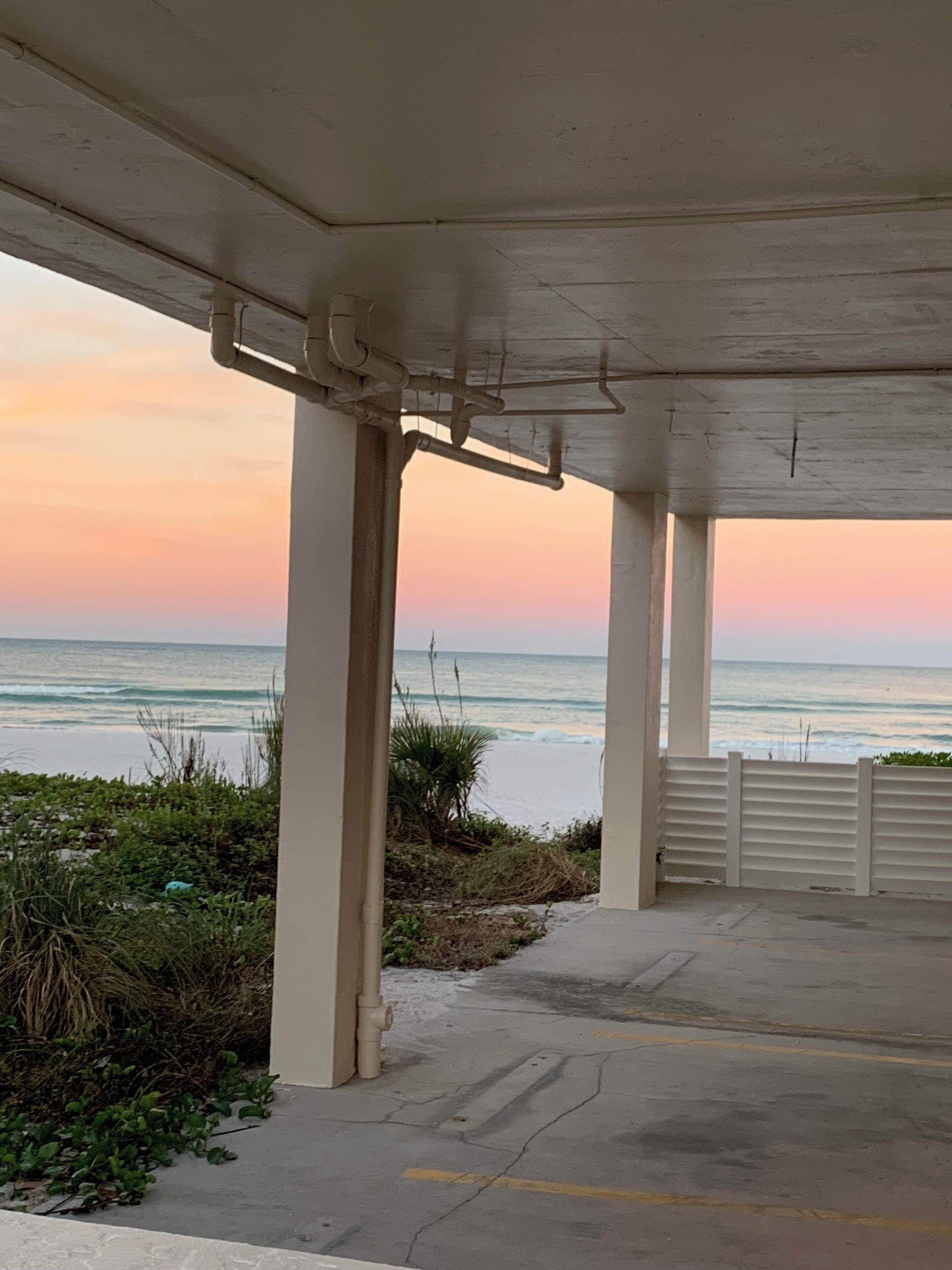 A covered outdoor area with concrete pillars, a view of the ocean, and a concrete floor with yellow lines.