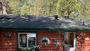 Une cabane rustique en rondins de bois, avec un toit végétalisé, un porche et une enseigne sur laquelle on peut lire « The Mays ».