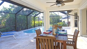 Eine sonnendurchflutete Terrasse mit Pool, Holztisch und Stühlen sowie einem Deckenventilator.