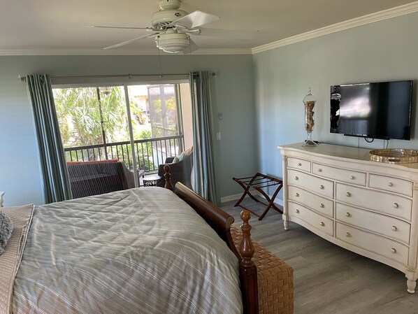 Un dormitorio con cama, cómoda, televisor y balcón con cortinas.