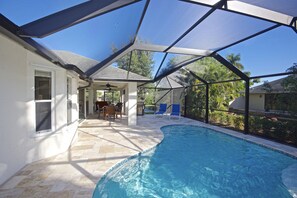 Una piscina cubierta con zona de terraza, ventilador de techo y vistas del paisaje circundante.