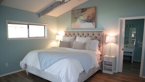 A bedroom with a bed, bedside lamps, a window, and a painting on the wall.