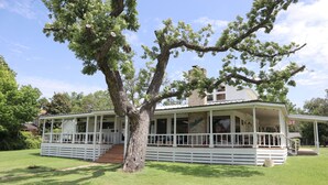 A white building with a porch, surrounded by grass and trees.