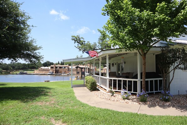 A covered outdoor area with a view of a lake, a white building with a porch, and an American flag.