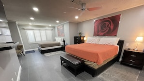 Un dormitorio moderno con una cama grande, un banco, un escritorio y un ventilador de techo.