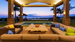 An outdoor seating area with a stone floor, cushioned sofas, and a central table with a bowl of snacks.