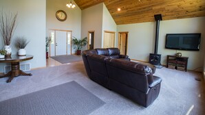 Ein geräumiges Wohnzimmer mit Ledersofa, Holzboden, Kamin und Fernseher.