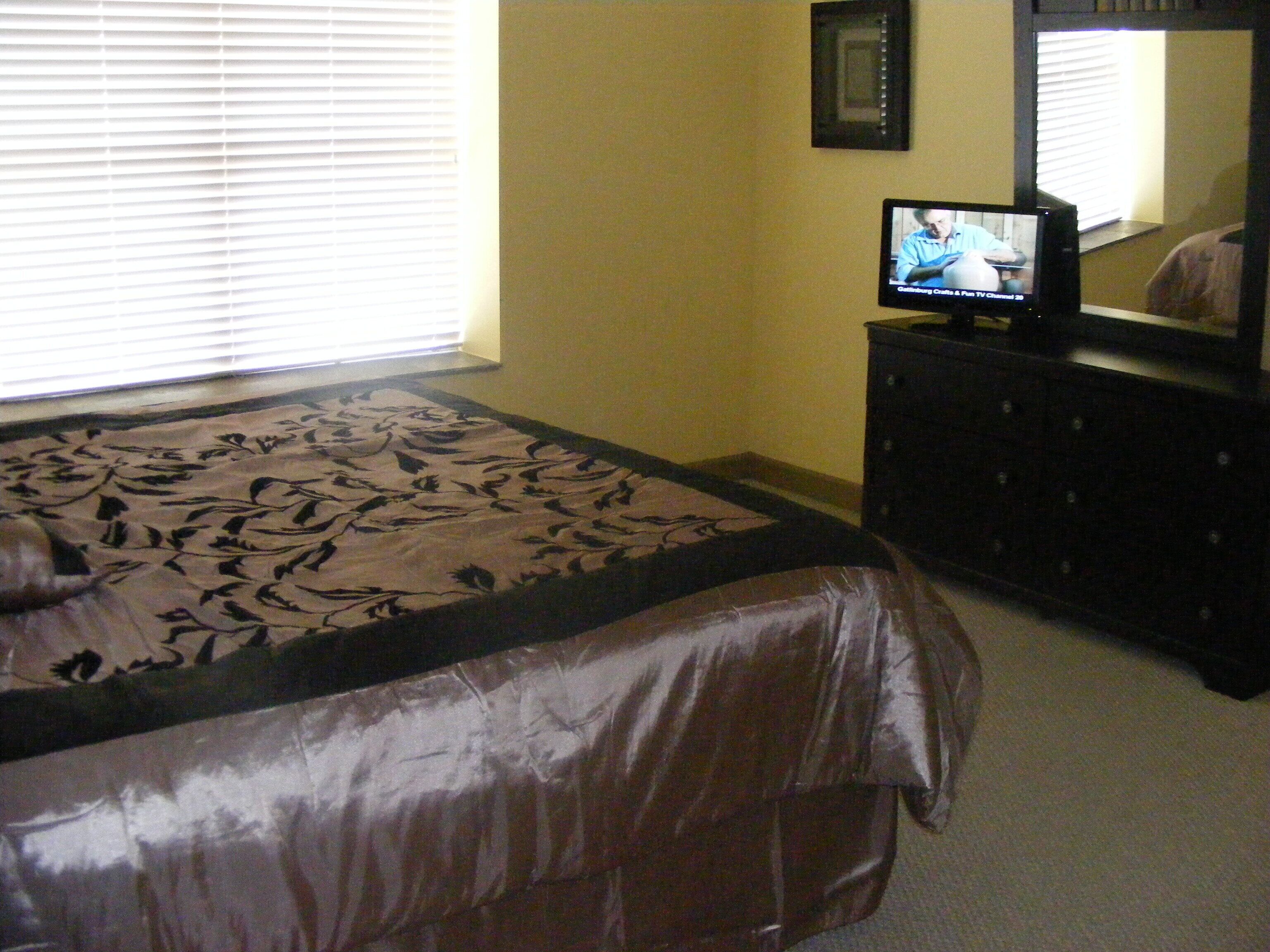 A bedroom with a bed, a dresser, and a television on a dresser.