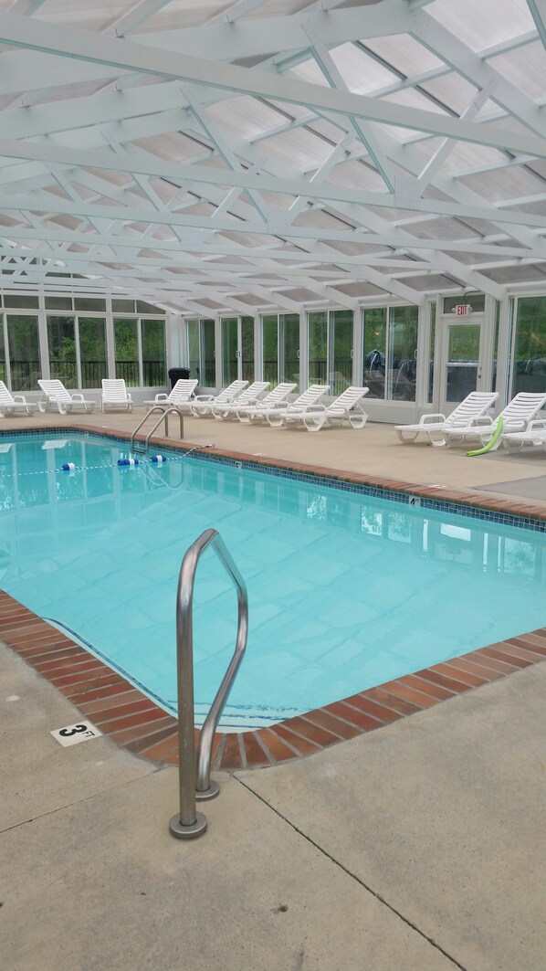 An indoor swimming pool with clear glass walls, white lounge chairs, and a marked depth of 3 feet.