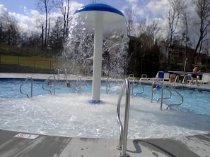 A swimming pool with a water fountain feature, surrounded by a deck with metal railings.