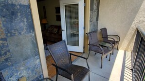 Un balcón con mobiliario de mimbre, una puerta que da a una habitación y vistas al exterior.