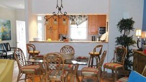 A dining area with wicker chairs, a glass table, and a hanging light fixture. - 'Beneath The Branches' Cottage Steps to Golf and Tennis. Pet-Friendly! (Murrells Inlet)