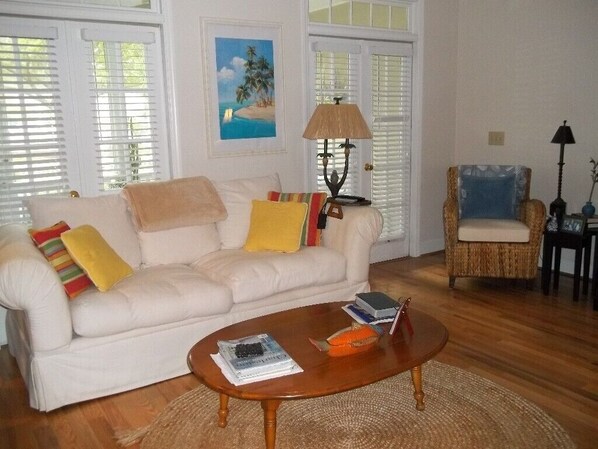 A living room with a white sofa, a wooden coffee table, and a wicker chair.