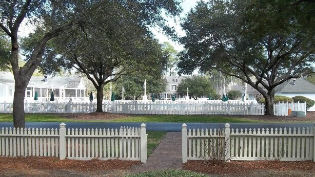 A park with white picket fences, trees, and a pathway leading to a building with a covered porch. - 'Beneath The Branches' Cottage Steps to Golf and Tennis. Pet-Friendly! (Murrells Inlet)