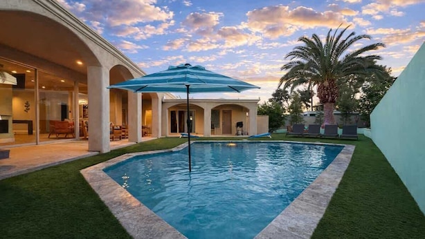 Una piscina con un paraguas azul, un patio con sillas y una palmera.