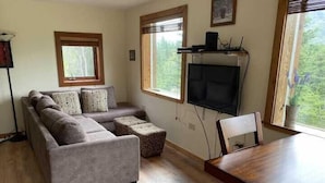 Una sala de estar con sofá, otomanas, televisor y una mesa de comedor.