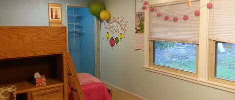 A room with a bunk bed, a desk, a chair, a window with blinds, and wall decorations including balloons and a tree mural.