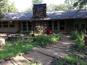 A stone building with a chimney, a gravel pathway, and a small garden area with plants and a bird feeder.